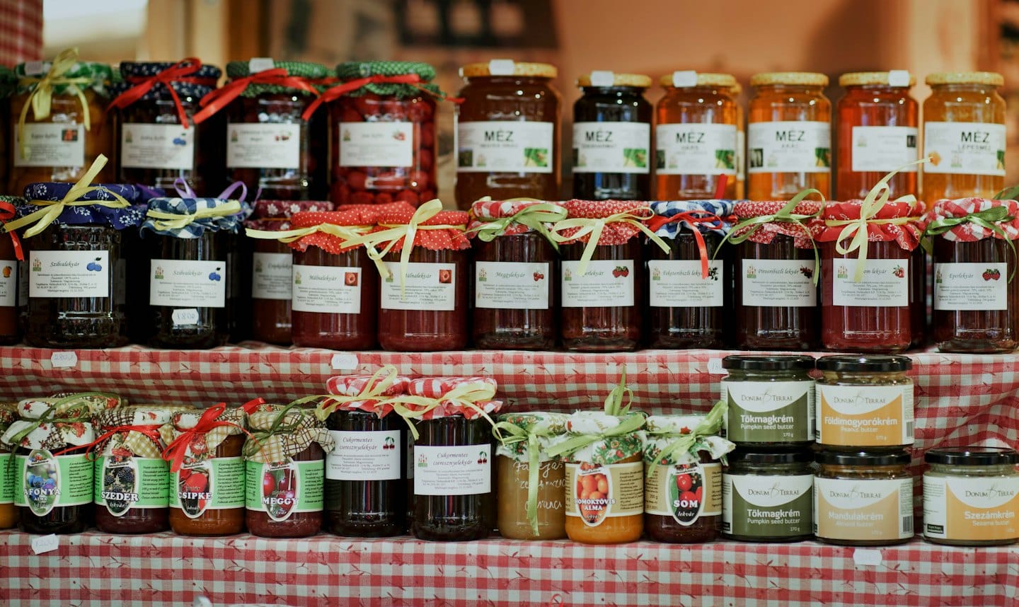 Artisan jars of honey, jams, and nut butters on checkered tablecloth.